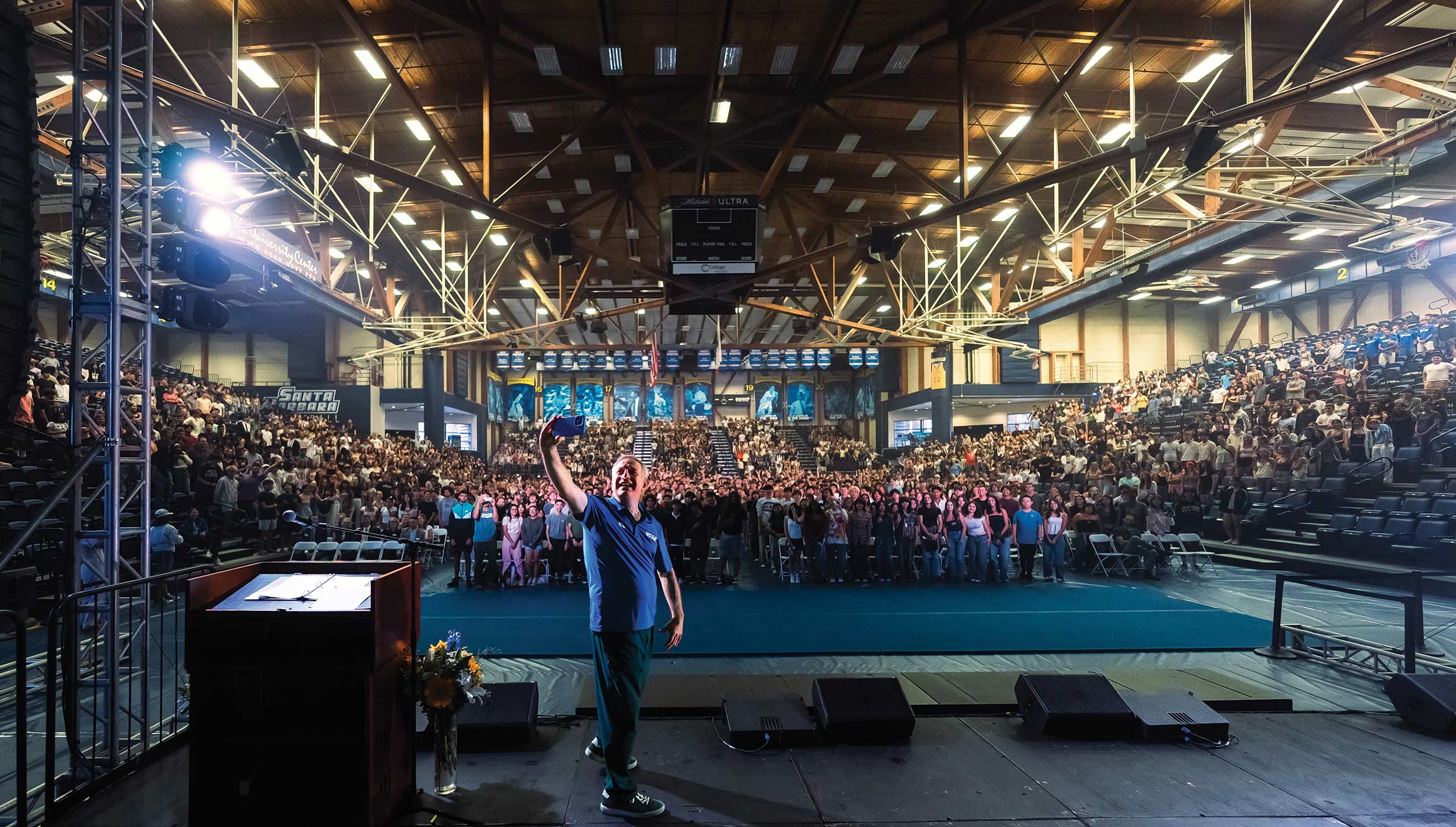 Chancellor Dennis Assanis takes a selfie on stage in the thunderdome with a crowd of students behind him.
